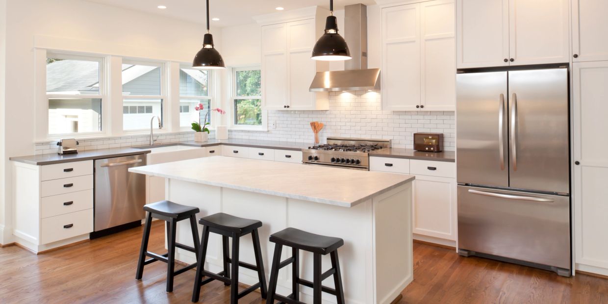 Cocina moderna blanca con isla central y taburetes negros.