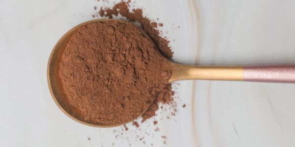 Golden spoon filled with cocoa powder on a white surface.