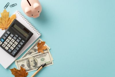 Calculator, piggy bank, money, and autumn leaves on blue background.