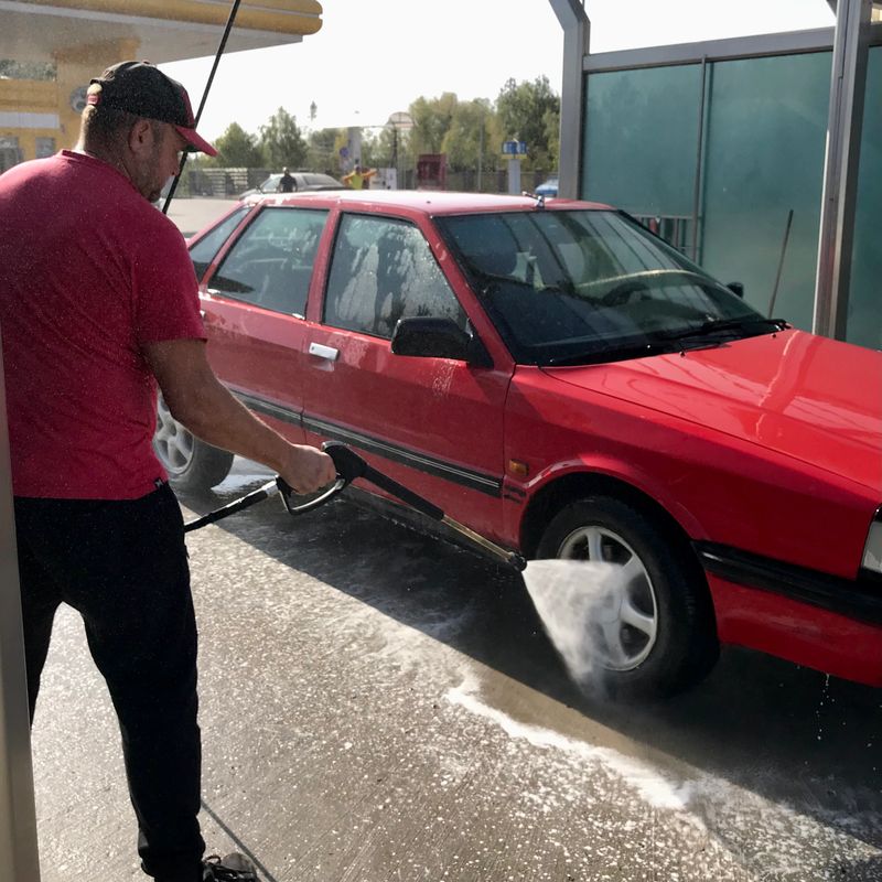 A man washes a red car at a car wash with detergent