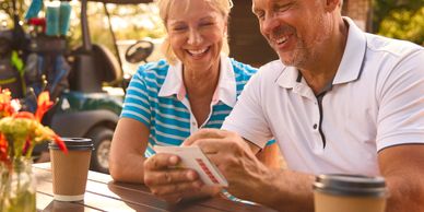 A happy couple playing cards outdoors at a sunny table.