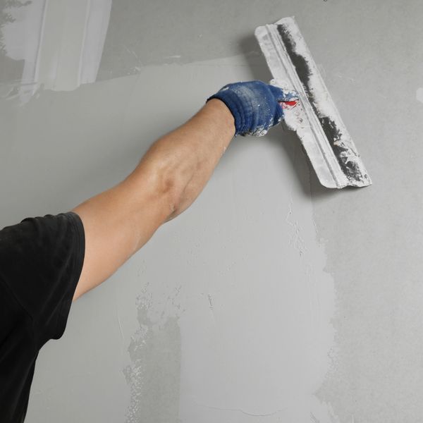 Hand applying plaster on a wall with a trowel.