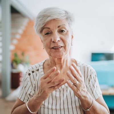 Elderly woman speaking with expressive hand gestures.