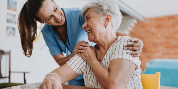 Smiling elderly woman with a caring nurse embracing her warmly.