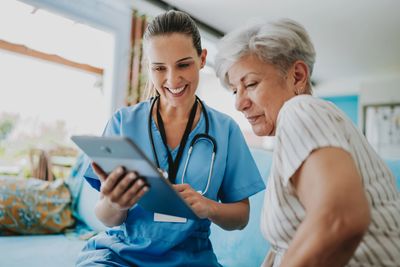 Young nurse showing tablet to elderly woman, both smiling.