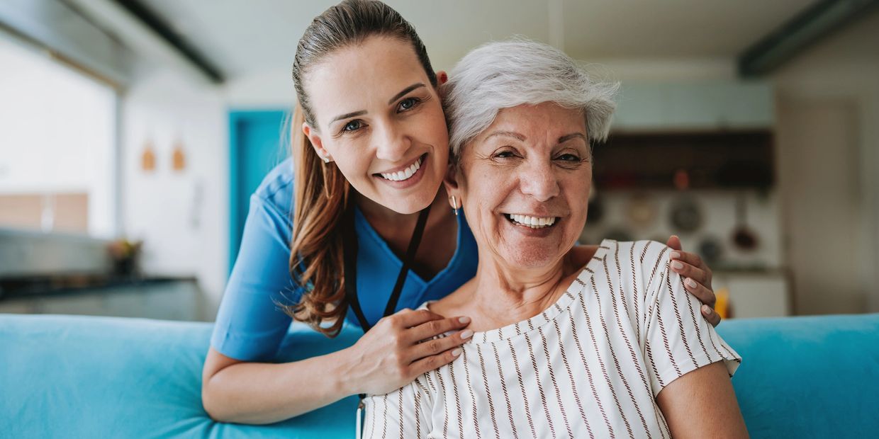 Happy female caregiver assisting a smiling senior client at home with in-home care services.