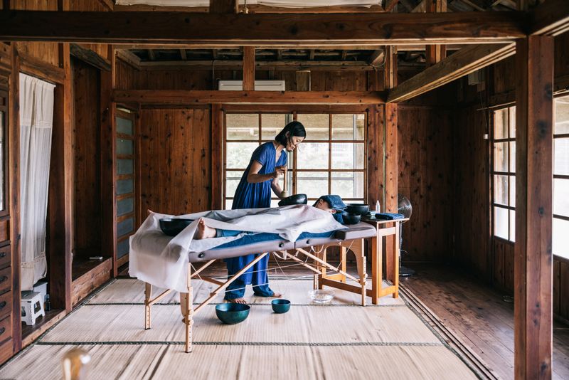 Wide shot captures the serene therapy room, where a therapist uses healing sound bowls to create a tranquil and therapeutic atmosphere for her client.