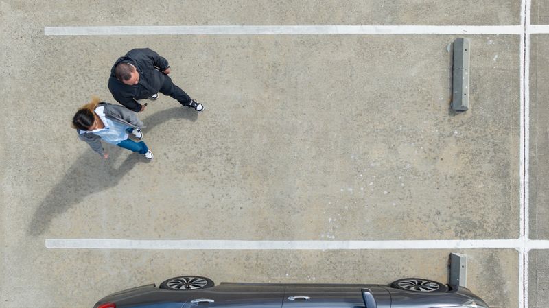 Aerial view, looking down at an authentic Asian American father teaching his daughter how to drive in an empty parking lot.