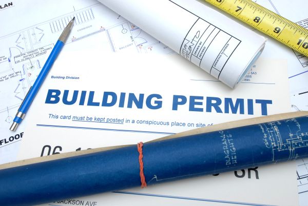 Building permit documents with blueprints and measuring tape.