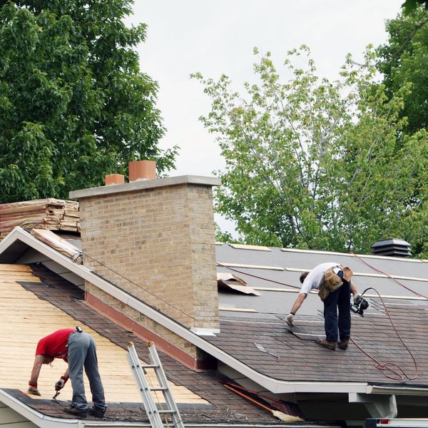 Two workers installing shingles on a roof under a cloudy sky.