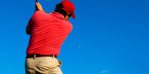 Golfer in red shirt hitting a golf ball under clear blue sky.