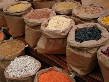 Various grains and legumes displayed in brown paper bags at a market.