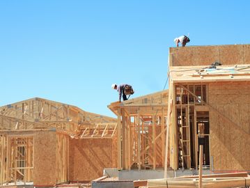 Workers constructing wooden frame houses under clear blue sky.
