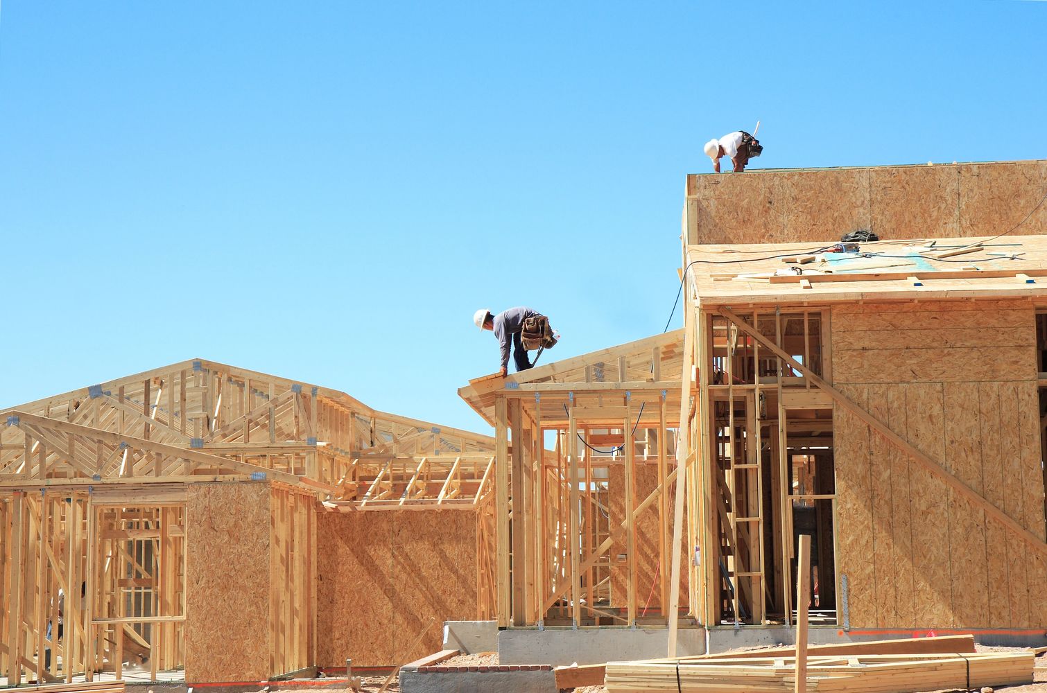 Construction workers building wooden framed houses under clear blue sky.