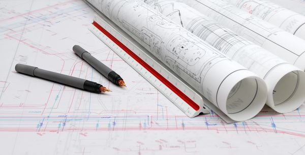 Architectural blueprints with pens and a scale ruler on a desk.