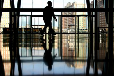 Silhouette of a person walking inside a building with reflective floors and large windows.