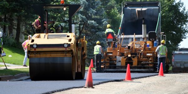 Workers paving a road using heavy machinery and roller.
