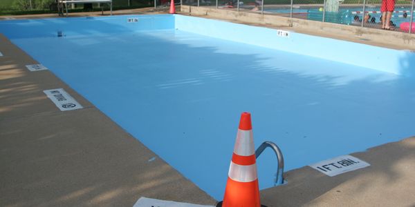 Empty swimming pool with a traffic cone and no diving signs around it.