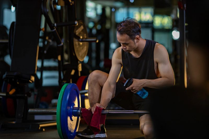 Asian staff trainer is doing daily cleaning the barbell in his gym for cleanliness and sanitize for hygiene and disease infection prevention process