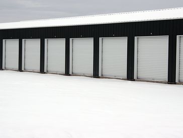 Row of closed white garage doors on a black building in snow.