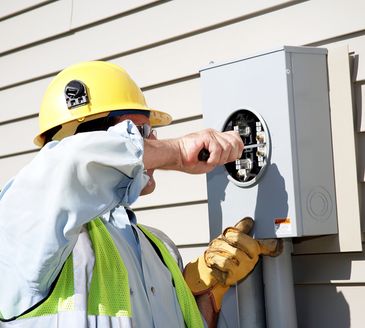 Two electricians working on an electrical panel, wearing safety helmets.