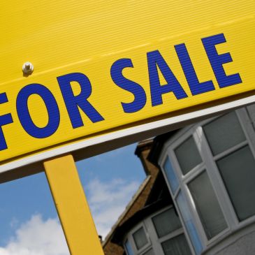 Yellow 'For Sale' sign in front of a house.