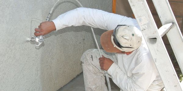 Painter applying textured paint with a spray gun on an exterior wall.
