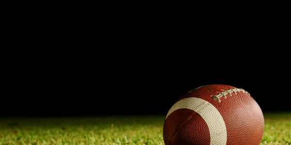 American football lying on grass with dark background.