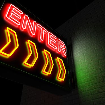 Bright neon sign displaying 'ENTER' with yellow arrows pointing right on a dark background.
