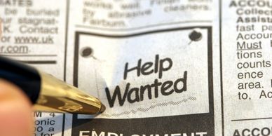 Close-up of a pen pointing at a 'Help Wanted' ad in a newspaper.