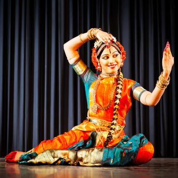 A traditional Indian dancer in vibrant attire performing a classical pose on stage.