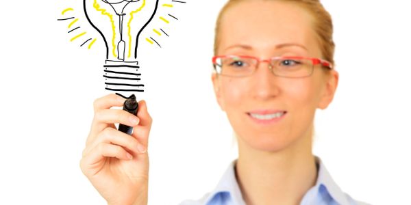 Woman in glasses drawing a glowing light bulb, symbolizing a new idea.