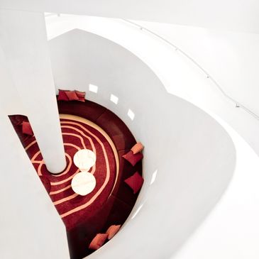 Modern curved seating area with red cushions and two round white tables.
