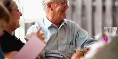 Elderly man smiling and enjoying conversation at a social gathering.