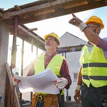 Two construction workers discussing plans on site during sunset.