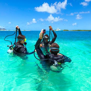 Three scuba divers preparing in clear turquoise water under a sunny sky.