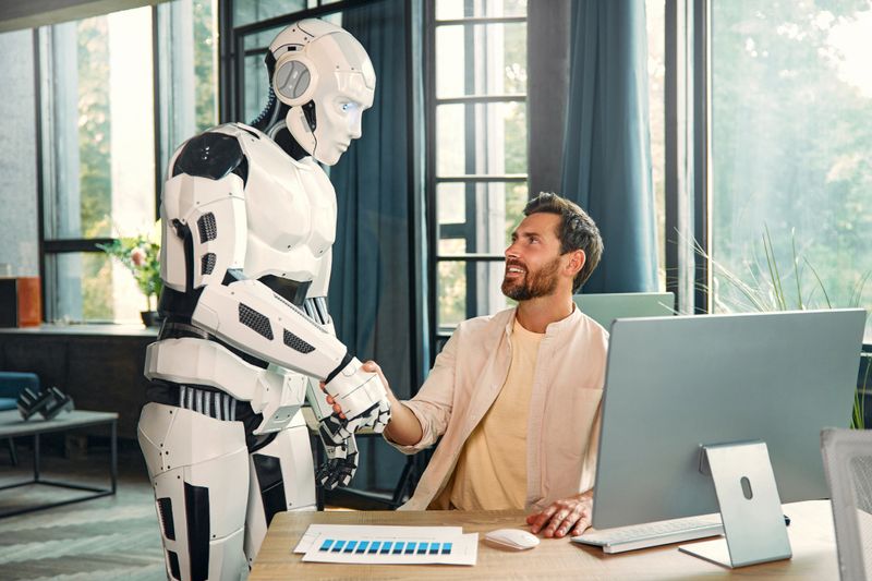 Robot assistant and young businessman working at a computer in a modern office. Collaboration between humans and artificial intelligence.