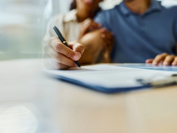 Person signing a document with another person beside them.
