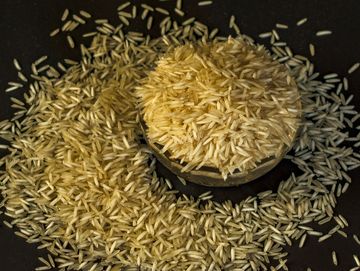 A pile of uncooked rice grains on a dark surface.