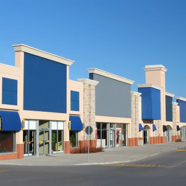 Empty retail storefronts in a modern shopping center under clear blue sky.