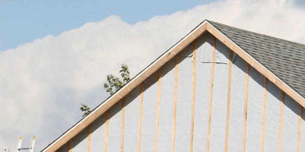 Two workers install siding on a house's exterior wall using scaffolding.