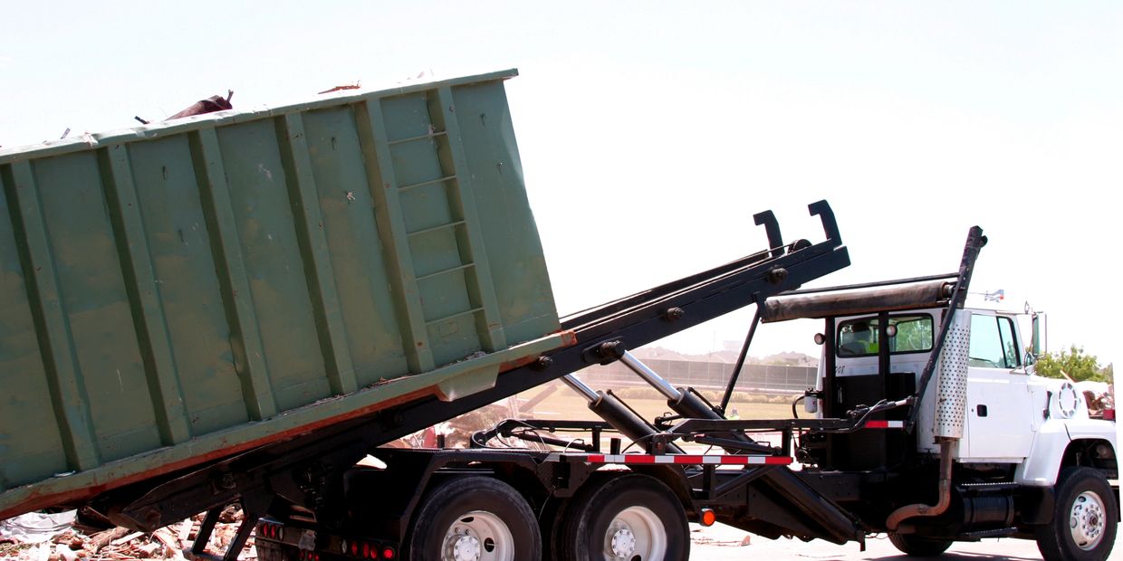 White truck unloading a green dumpster container.