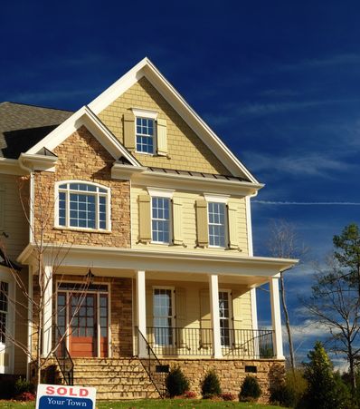 Beautiful two-story house with a sold sign in front under a deep blue sky.