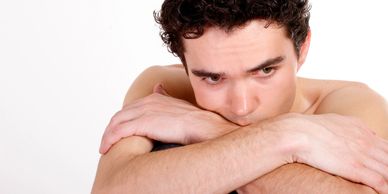 Pensive young man resting his head on crossed arms, appearing deep in thought.