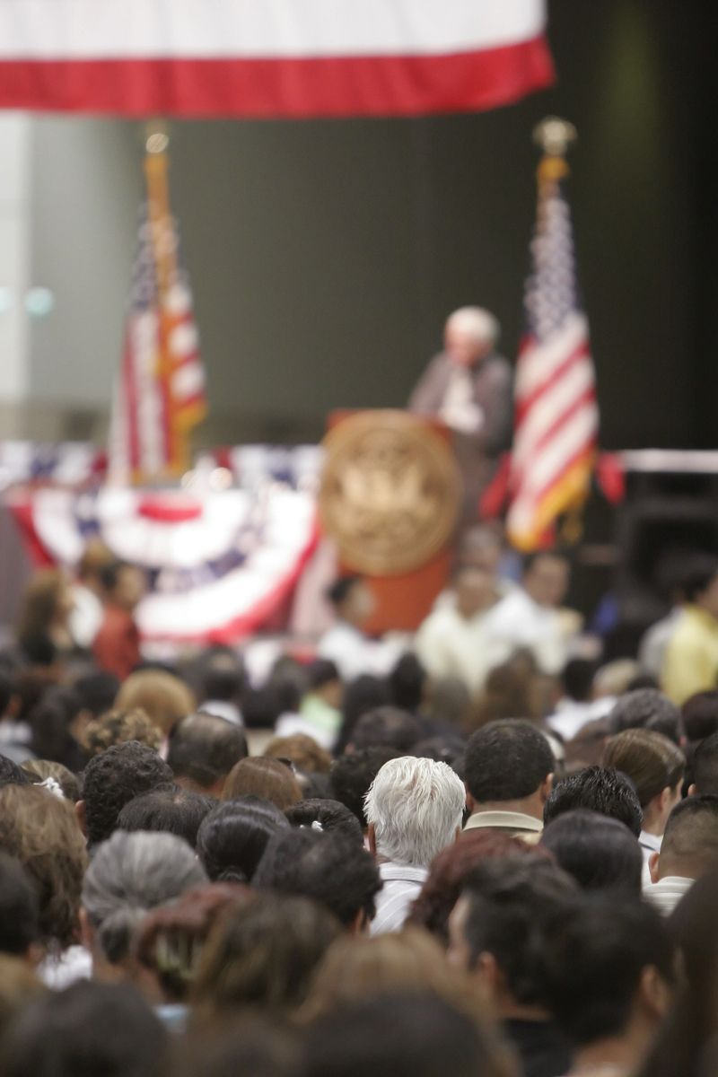 Focus on an audience member listening intently at a large town hall meeting/swearing-in ceremony.