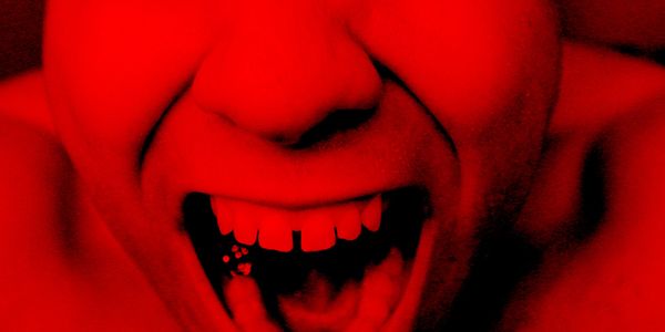 Close-up of a person shouting or screaming under intense red lighting.