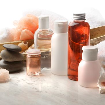 Assorted spa and bath products on a marble surface with towels and stones.
