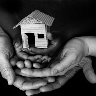 Hands holding a small cardboard house, symbolizing care and protection.
