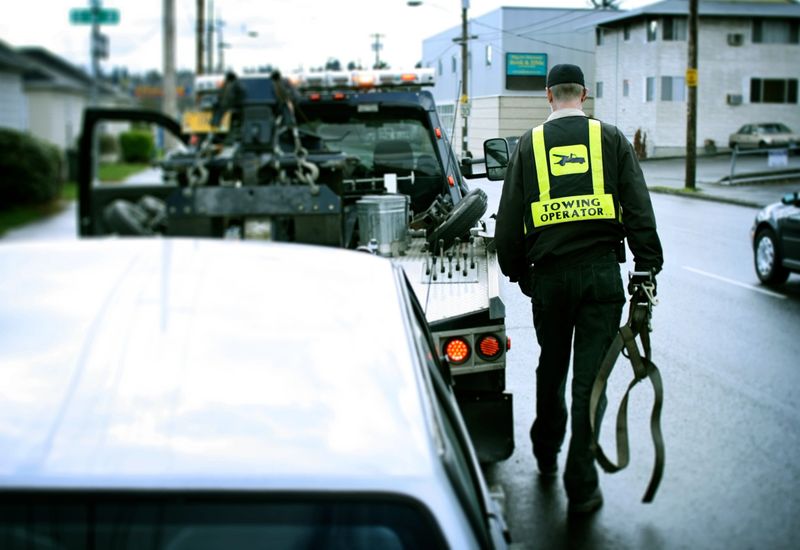 A road side assistance professional on the job hooking up a broken down car to his tow truck.  Horizontal with copy space.