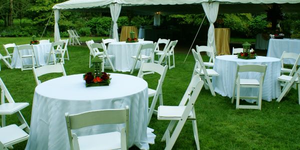 Outdoor event setup with round tables and white chairs.